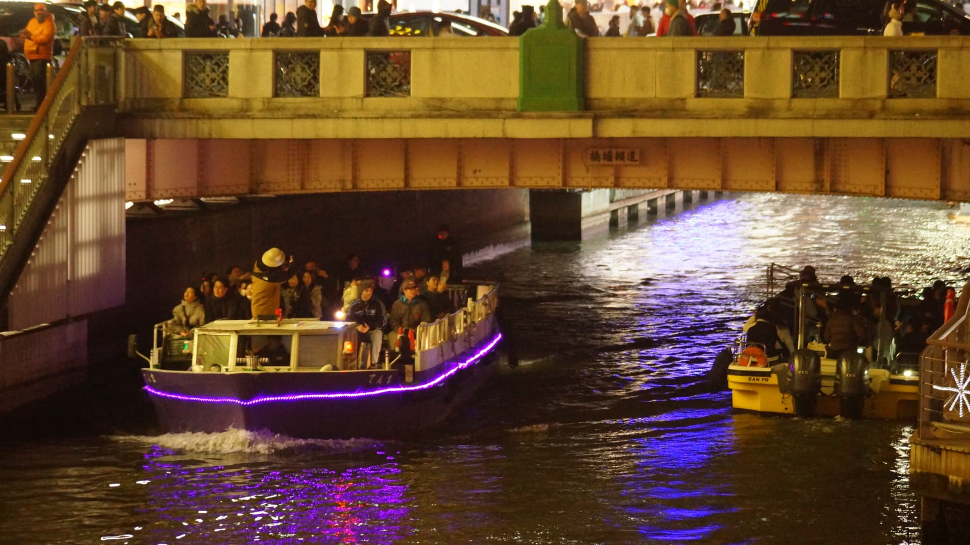 Night cruise boats passing under a bridge on the Dotonbori canal